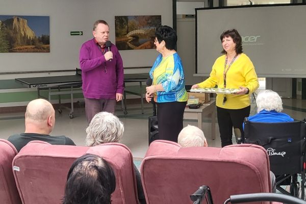 Pani Dyrektor, przewodniczący i Pani Kierownik rozdaje jajko  Mieszkańcom zgromadzonym na holu domu.