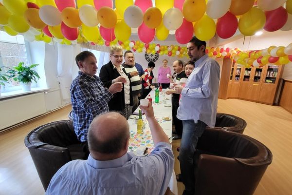 Mieszkańcy wznoszą toast na stojąco przy długim stole.