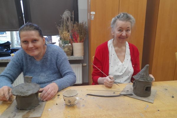 Dwie panie lepią z gliny domek.