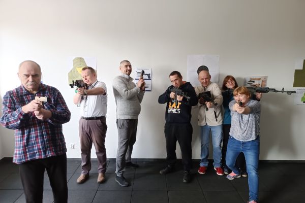 Grupa mieszkańców celuje z broni na zdjęciu grupowym.