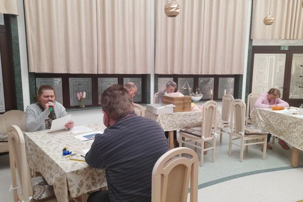 Mieszkańcy wykonują różne rzeczy w sali terapii zajęciowej siedząc przy stolikach.