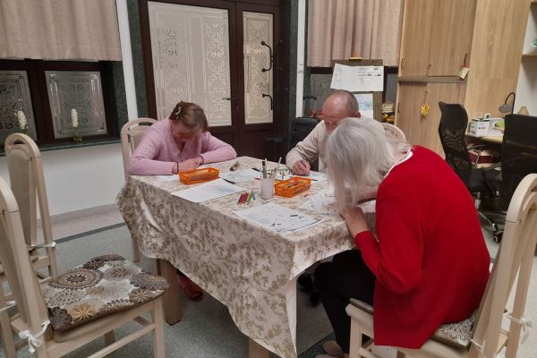 Mieszkańcy wykonują różne rzeczy w sali terapii zajęciowej siedząc przy stolikach.