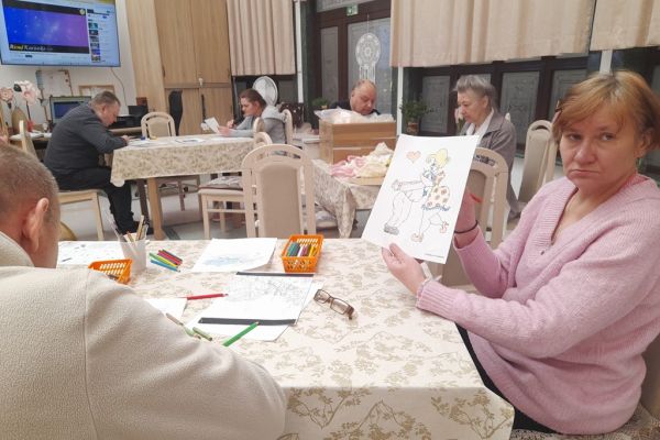 Mieszkańcy wykonują różne rzeczy w sali terapii zajęciowej siedząc przy stolikach.