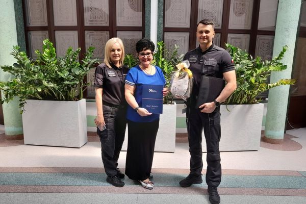 Pani Dyrektor Domu i Pan Dyrektor i pracownica Aresztu na holu domu trzymaja porozumienie współpracy, stojąc na holu domu.