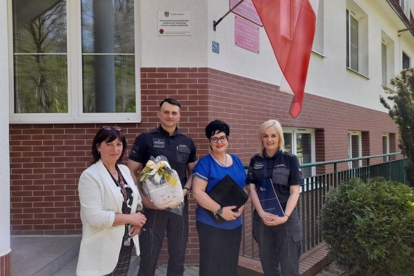 Pani Dyrektor i Kierowniczka Domu i Pan Dyrektor i pracownicaAresztu na holu domu trzymaja porozumienie współpracy stojąc przed budynkiem Domu.