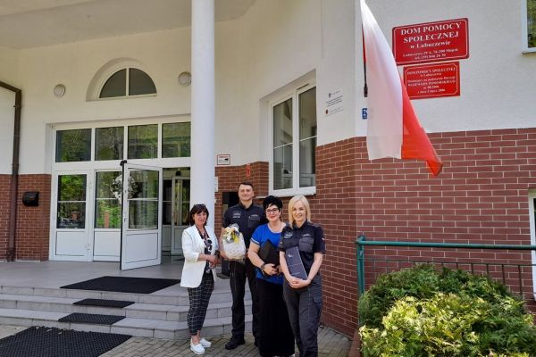 Pani Dyrektor i Kierowniczka Domu i Pan Dyrektor i pracownicaAresztu na holu domu trzymaja porozumienie współpracy stojąc przed budynkiem Domu.