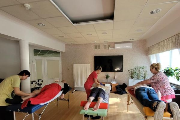 Kilkoro mieszkańców na dużej sali w domu mają wykonywany masaż na leżąco przez ucznów szkoły.