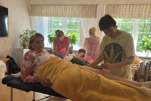 Kilkoro mieszkańców na dużej sali w domu mają wykonywany masaż na leżąco przez ucznów szkoły.