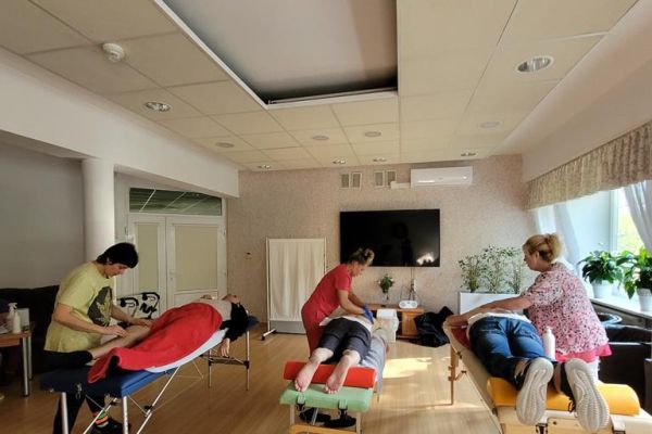 Kilkoro mieszkańców na dużej sali w domu mają wykonywany masaż na leżąco przez ucznów szkoły.