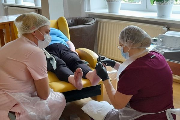 Panie podolog wykonują zabieg na stopach mieszkanki.