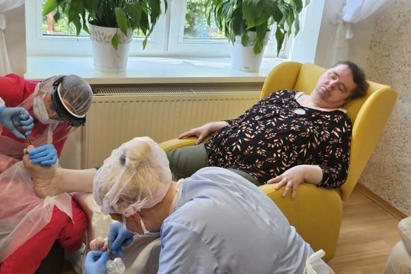 Panie podolog wykonują zabiegi na stopach mieszkanki.