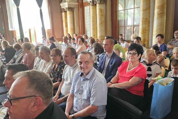 Mieszkańcy i inni uczestnicy uroczystoąści siedzą i oglądają widowisko.