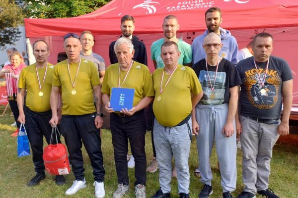 Grupowe zdjęcie mieszkańców z medalami i znanymi sportowcami.