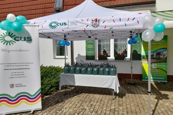 Dwa rolapy informacyjne i stół z torebkami z kwiatami w podziękowaniu dla uczestników.