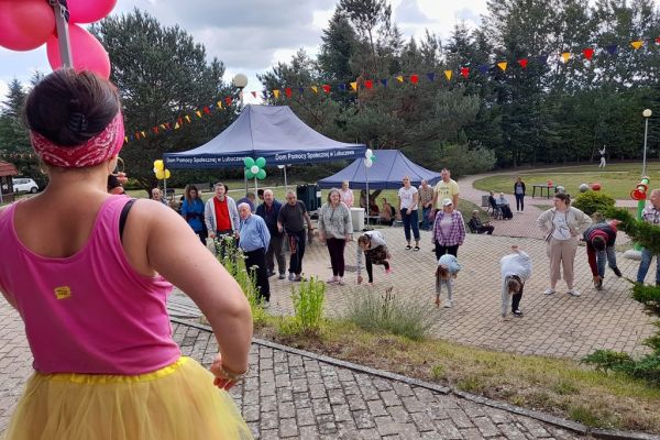 Uczestnicy pikniku tańczą na polbruku, na pierwszym planie animatorka zabaw.