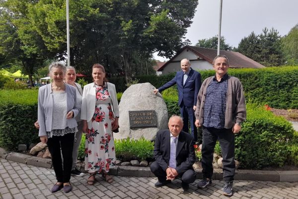 Pięcoro mieszkańców przy pamiątkowym głazie z tablicą informacyjna z uroczystości.