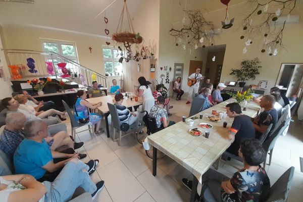 Uczestnicy pikniku w sali ŚDS w Motarzynie siedzą i śpiewają piosenki a instruktor gra na gitarze.
