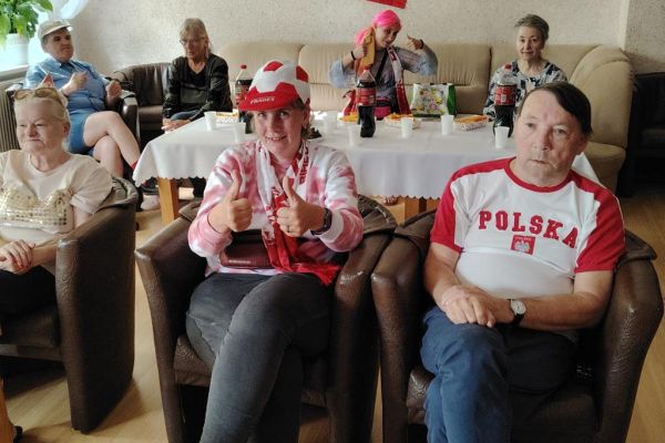 Mieszkańcy w sali kawiarnianej oglądaja mecz i kibicują w strojach biało czerwonych.