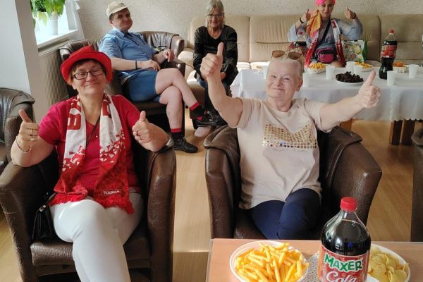 Mieszkańcy w sali kawiarnianej oglądaja mecz i kibicują w strojach biało czerwonych.