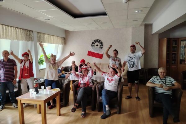 Mieszkańcy w sali kawiarnianej oglądaja mecz i kibicują w strojach biało czerwonych.
