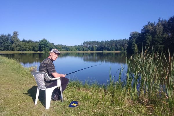 Mieszkaniec łowi ryby nad jeziorem na wędkę.