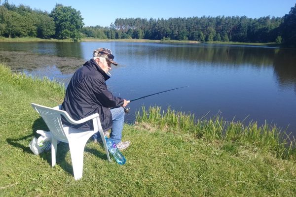 Mieszkaniec łowi ryby nad jeziorem na wędkę.