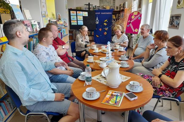 Mieszkańcy siedzą przy stolikach w bibliotece.