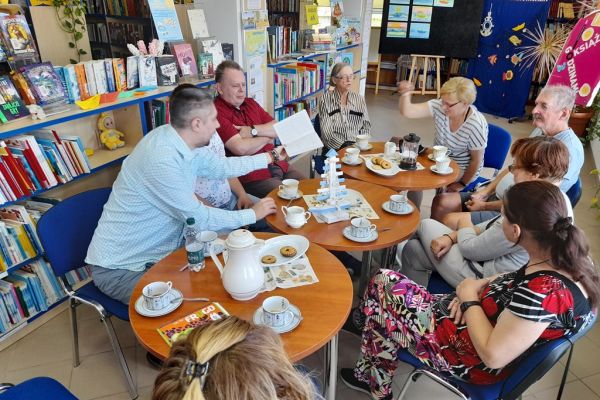 Mieszkańcy siedzą przy stolikach w bibliotece.