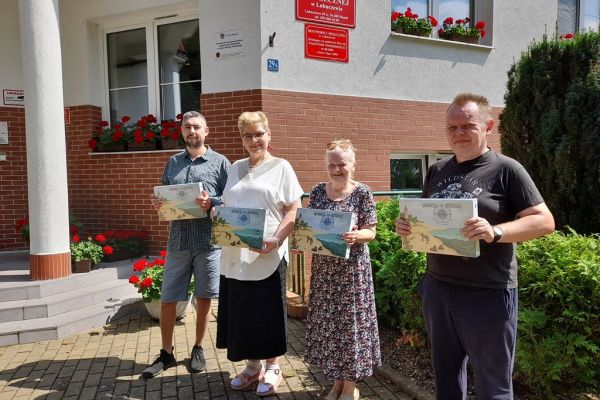 Czworo mieszkańców trzyma nagrody stojąc na tle domu.