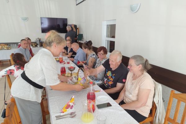 Mieszkańcy siedza przy długim stole na świetlicy.