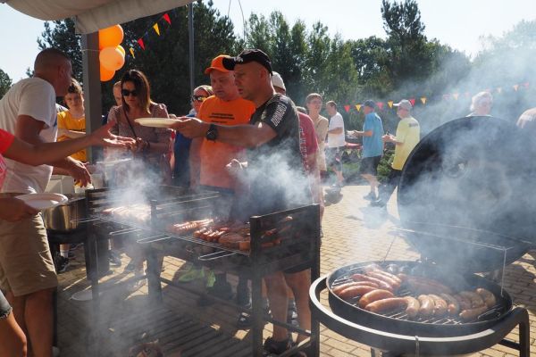 Uczestnicy częstowani kiełbaska przy grillu.