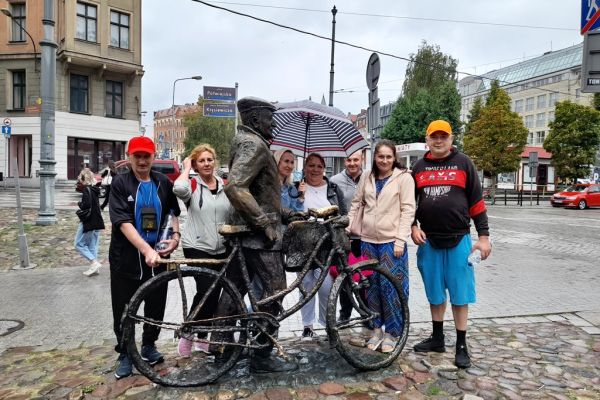 Grupka mieszkańców i opiekunów przy pomniku w Poznaniu.