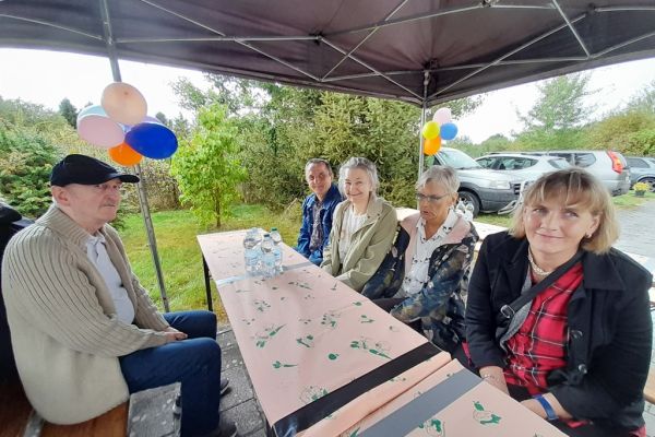 Kilkoro mieszkańców siedzą pod namiotem na festynie.