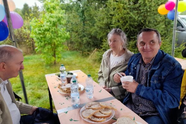 Kilkoro mieszkańców siedzą pod namiotem na festynie.