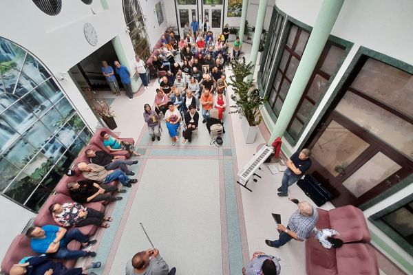 Mieszkańcy siedza na holu domu i słuchaja koncertu w wykonaniu gości.