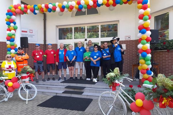 Władze placówek i powiatu ustawieni w rzędzie na tle wejścia do domu udekorowanego balonami.