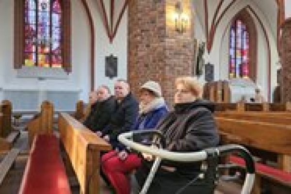 Pięcioro mieszkańców siedzi w ławce w kościele.