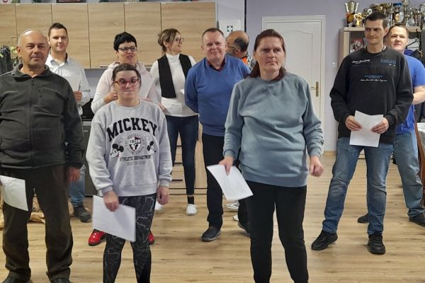Mieszkanka wśród innych uczestników próby wokalnej śpiewa razem z nimi na stojąco.