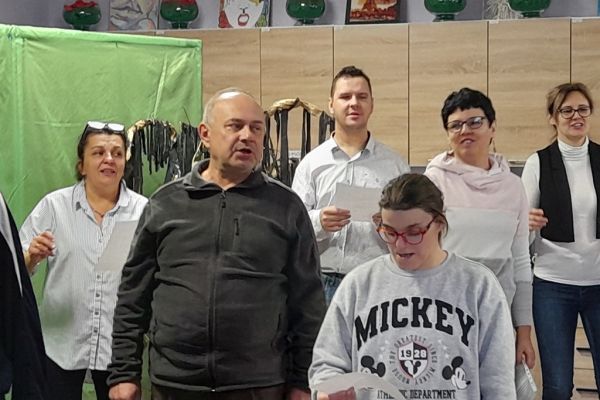 nasz mieszkaniec i inni uczestnicy próby wokalnej śpiewają piosenkę stojąc.