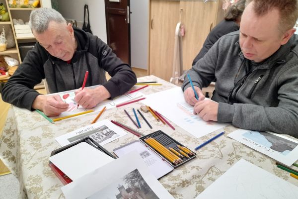 Mieszkańcy rysują przy stoliku.