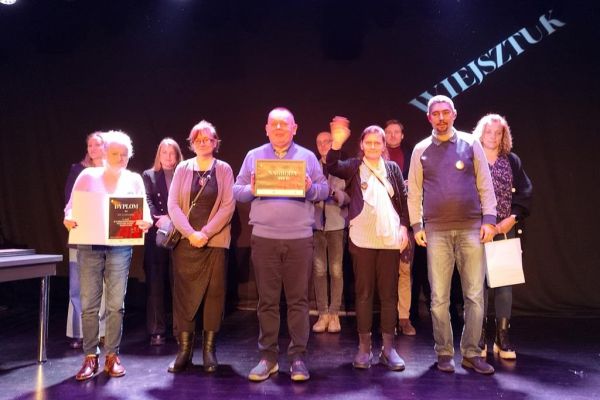 Grupowe zdjęcie mieszkańców podczas odbioru nagrody na scenie.