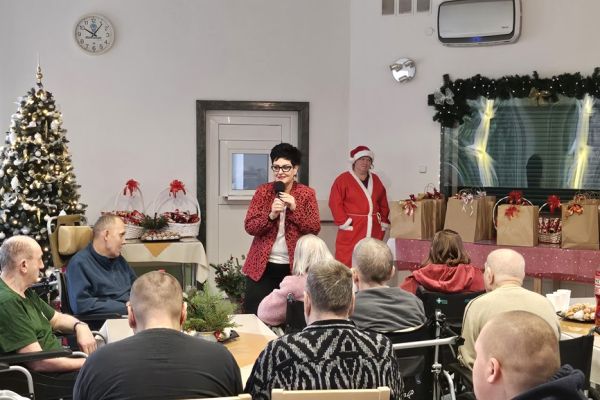 Siedzący mieszkańcy słuchają Pani Dyrektor mówiącej przez mikrofon.