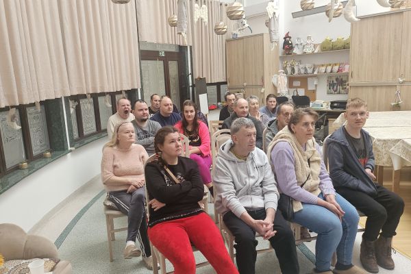 Mieszkańcy siedzą na krzesłach i oglądają film.