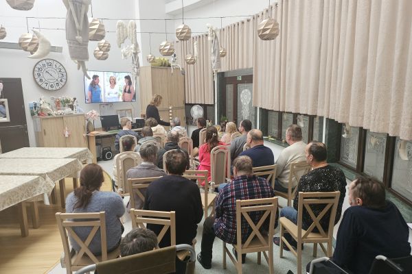 Mieszkańcy siedzą na krzesłach i oglądają film.