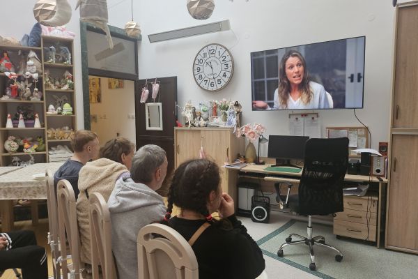 Mieszkańcy siedzą na krzesłach i oglądają film.