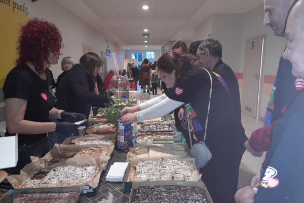 Mieszkańcy wrzucają pieniądze do puszki Wośp przy stole suto zastawionym ciastami.