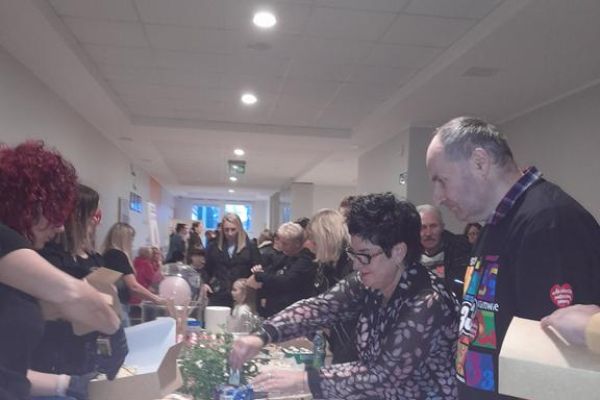 Mieszkańcy i Pani Dyrektor wrzucają pieniądze do puszki przy stole suto zastawionym ciastami.