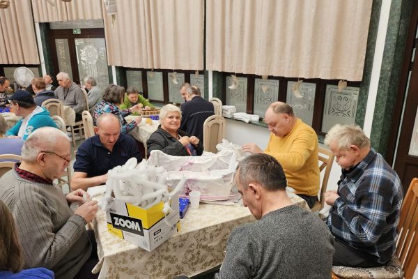 Mieszkańcy w sali terapii siedzą i wykonują różne prace manualne przy stolikach.