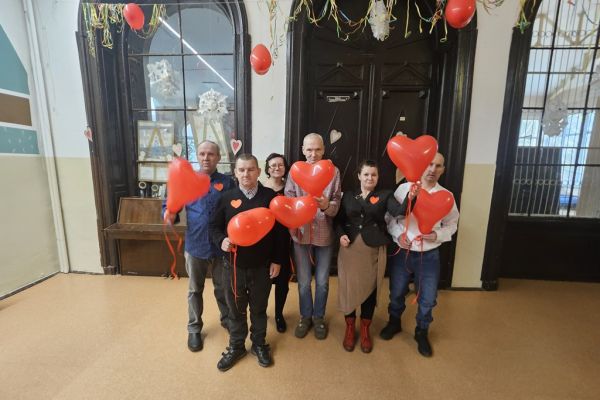 Mieszxkańcy w zdjęciu grupowym trzymają czerwone balony w kształcie serc.