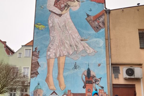 Mieszjkańcy stoja przy muralu na budynku.